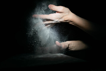 Obraz na płótnie Canvas closeup of hand sprinkling flour on table with black background córdoba argentina