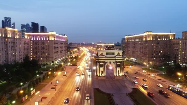 Moscow, Russia. Aerial view of the new triumphal arch, car traffic and city buildings. Illuminated skyscrapers on the horizon. Taken by drone at evening