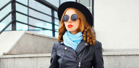 Portrait of beautiful young woman model wearing a black round hat, jacket, sunglasses in the city