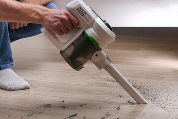 A man uses a bagless vertical cordless vacuum cleaner to clean the floor.