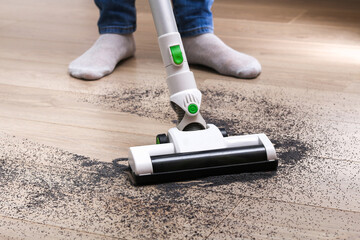 A man uses a bagless vertical cordless vacuum cleaner to clean the floor.