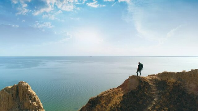 The male with big bag standing on the mountain cliff on the seascape background