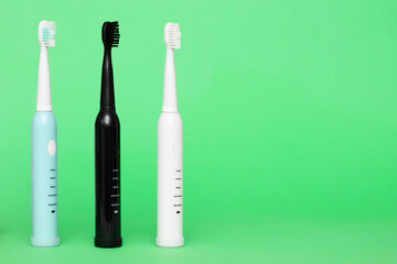 Electric wireless toothbrushes in blue, black and white on a light green background