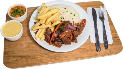 Peruvian food Lomo Saltado, French fries with meat, onion, yellow pepper, parsley, white rice and soy sauce, on a white plate with cutlery and wooden background.