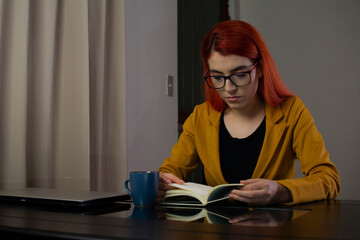 Woman reading a book with a cup of coffee after working from home
