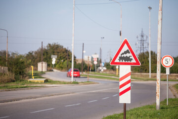 Typical European railroad crossing sign on a rural road indicating an unguarded level crossing soon, with its iconic black steam locomotive on a red triangle