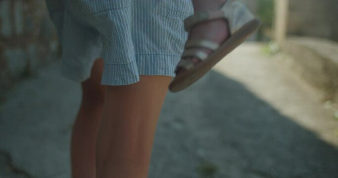 Tracking shot of the feet of a 2 years old cute little girl, held in the arms of her older sister in the streets of an old european town on a sunny day in summer