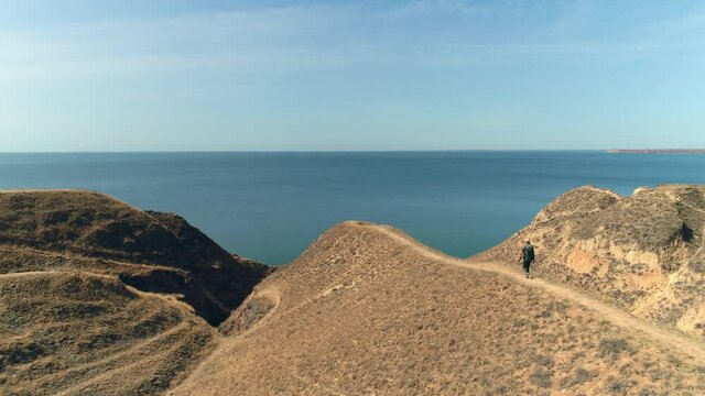 The man with backpack walks on the mountain range on the beautiful seascape