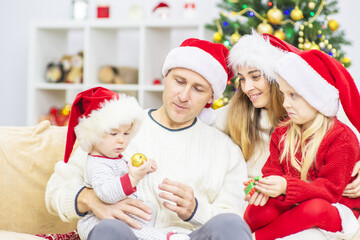 A family with children in santa hats are sitting at home on the sofa against the background of a Christmas tree and wish each other a Merry Christmas (New Year)