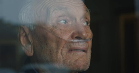 Cinematic close up shot of an elderly thoughtful man wearing oxygen tube is looking through a window in the morning. Concept of healthcare, life, pensioner, grandparents, retirement, boarding house. - Powered by Adobe