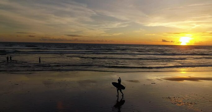 Drone video of surfer running down the beach with surfboard at sunset