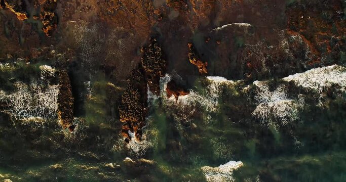 Top down drone video of waves breaking on rocky beach.
