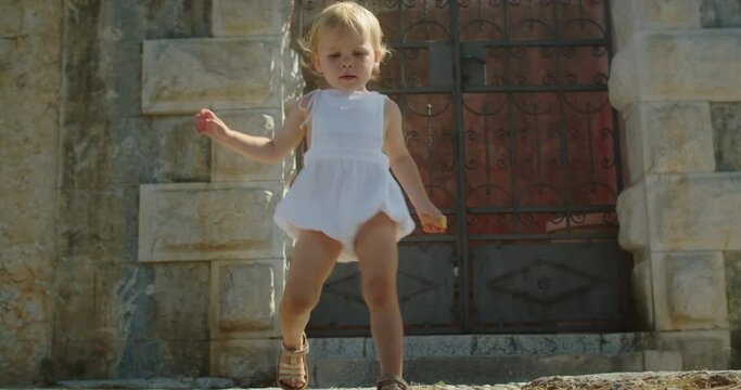 Cute 2 years old girl jumping on stone steps in an old european town on a sunny day in summer