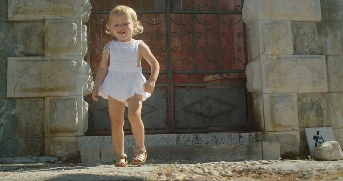 Cute 2 years old girl joyfully jumping on stone steps in an old european town on a sunny day in summer