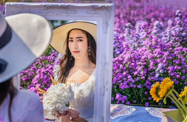  Beautiful woman looking in a mirror in a flower field in Chiang Mai, Thailand.