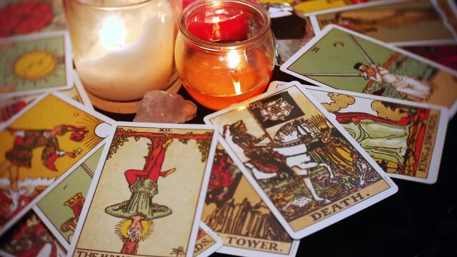 A mystical tarot deck of cards is displayed in a rotation. The hangman and death card are prominent. Candles and crystals are seen in the center of the table.