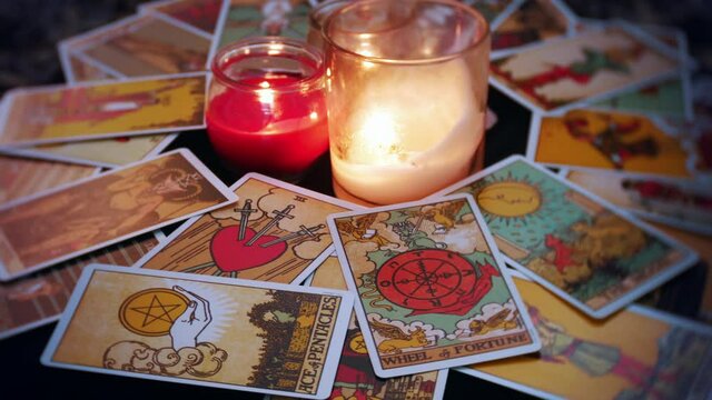 A mystical tarot deck of cards is displayed in a rotation. The wheel of fortune and moon card are prominent. Candles and crystals are seen in the center of the table.
