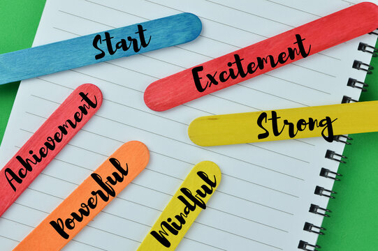 Top view of colorful ice cream sticks and notebook on a green background written with word START, EXCITEMENT, STRONG, MINDFUL, POWERFUL, ACHIEVEMENT. Motivational concept.