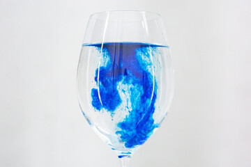 A drop of blue liquid was just poured into a clear wineglass