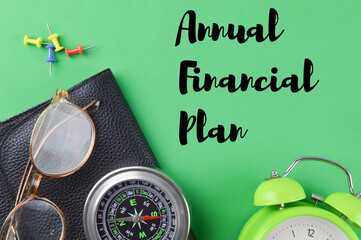 Flat lay view of clock, compass, glasses, black file and push pins on a green background written with text ANNUAL FINANCIAL PLAN. Business concept.
