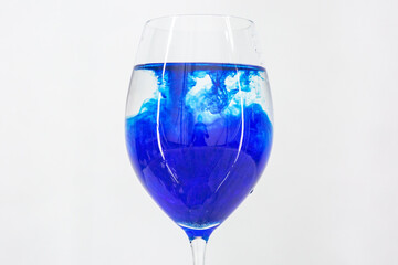 A drop of blue liquid was just poured into a clear wineglass