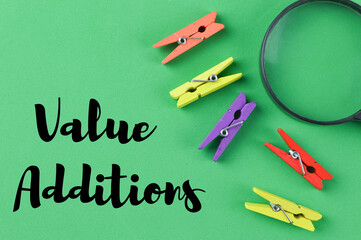 Top view of magnifying glass and wooden clips isolated on a green background written with text VALUE ADDITIONS. Business and education concept.
