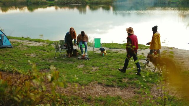 Near lake hipster friends met eath other sitting near lake. Four young people hug smiling with dog. Vacation tourism adventure outdoors. Close up. Slow motion
