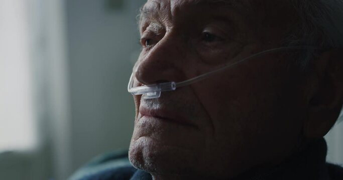 Cinematic close up shot of an elderly thoughtful man wearing oxygen tube is looking in camera. Concept of healthcare, life, pensioner, grandparents, retirement, boarding house.
