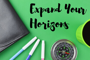 Selective focus of black file, colors, compass and a cup of coffee on green background written with text EXPAND YOUR HORIZONS. Business concept.