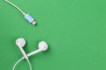 Top view of earphones and usb cable on a green background. Modern technology.