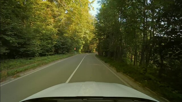 Driving by car through a curvy road at a beautiful day in summer, twi times speeded up - front window view over the engine hood.