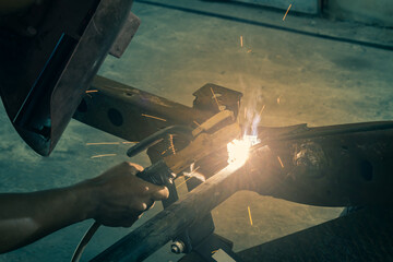Hand of Welding Worker Hold Welding Mask and Welding Metal or Steel Construction of Car in Garage in Vintage Tone