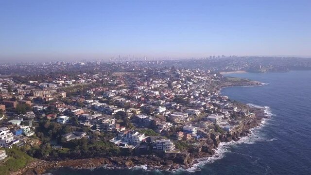 Aerial orbiting over coastal beach front houses with beautiful Sydney City CBD view in the background