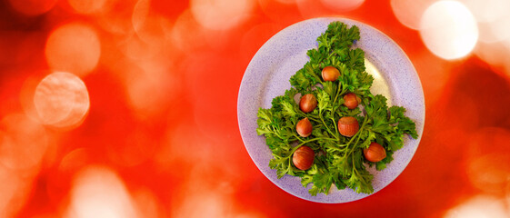 Christmas tree made of herbs and hazelnuts on a plate. New year decor from food. Isolated on a red background. Copy space