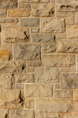 Full frame abstract background of an attractive tan brown natural limestone block wall in ashlar pattern, with rugged texture stone blocks in full sunlight with copy space