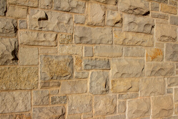 Full frame abstract background of an attractive tan brown natural limestone block wall in ashlar pattern, with rugged texture stone blocks in full sunlight with copy space