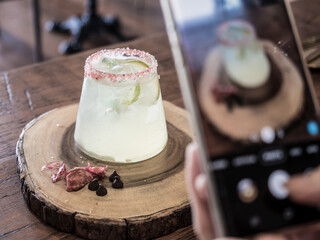 person using mobile smart phone taking photo of drink when served. beautiful cocktail decoration on wooden table. taking photo for social network.