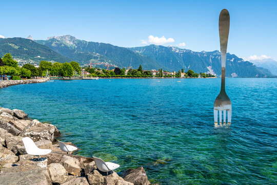Empty chairs on rocks on shore of Lake Geneva and world biggest fork Vevey Switzerland