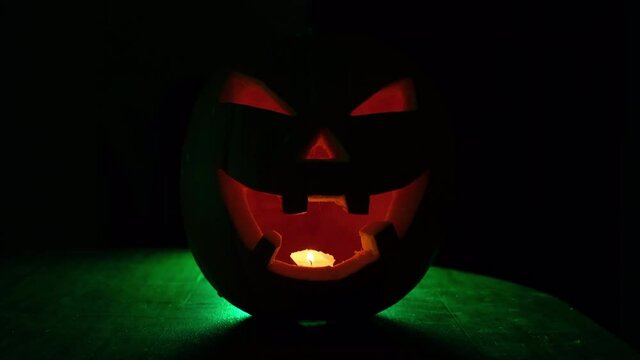 Halloween spooky pumpkin lantern in the dark. Green light in the background.