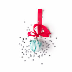 Christmas composition. A red ribbon with a bow is tied to a glass Christmas green ball. Confetti stars are scattered nearby. The concept of preparing for the new year and christmas. Flat lay.