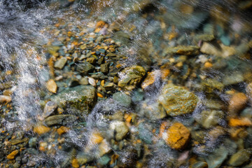Rocky bottom of mountain river through the clear water, selective focus, blurring the image. Cristal water in the stream shimmers in sunlight. Stone background.