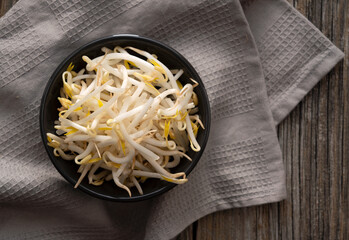 Bean sprouts and cloth in a black bowl set against an old wooden background