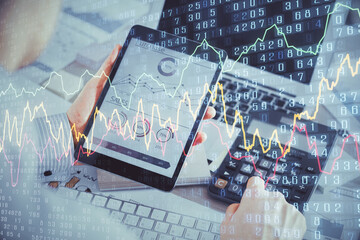 Double exposure of man's hands holding and using a digital device and forex graph drawing. Financial market concept.