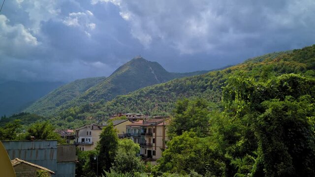 Town hidden in mountain woods, contrasting day light and clouds, Montello, Italy