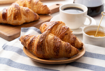 A croissant, and coffee and honey behind it