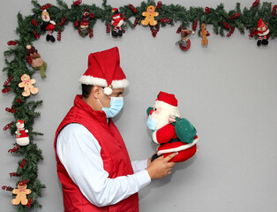 latin man with protection mask and santa claus doll in christmas decoration, new normal covid-19
