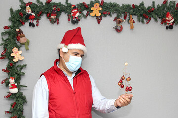 
Latin man with protection mask and Christmas tree with spheres in Christmas decoration, new normal...