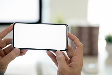 Cropped shot of man hand holding blank screen smartphone in bright modern office room.