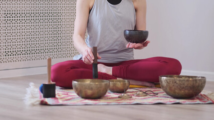 Woman playing on Tibetan singing bowl while sitting on yoga mat. Vintage tonned.