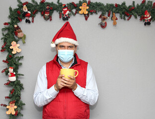 latin man with protection mask and cup of coffee in christmas decoration, new normal covid-19